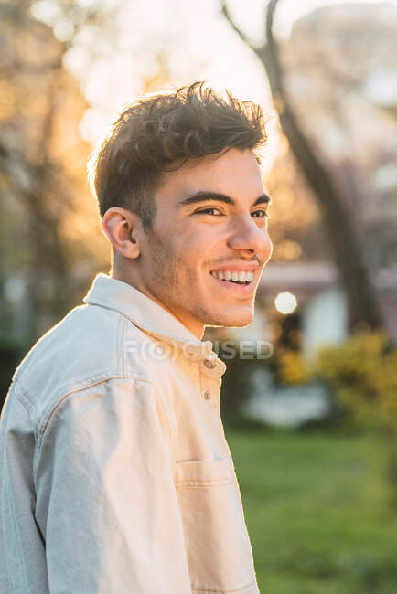 Vista laterale di un bel maschio felice che sorride mentre trascorre il fine settimana nel parco e distoglie lo sguardo — Foto stock