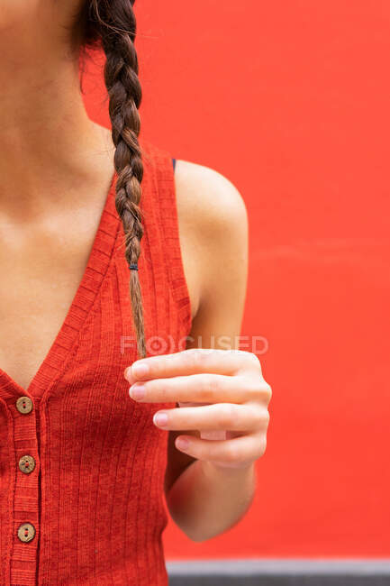 Обрізати молоду жінку, торкаючись косички на червоному тлі на вулиці — стокове фото