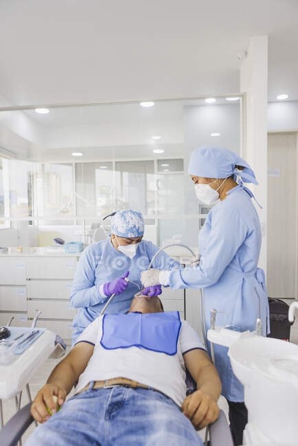 Estomatologista feminina tratando dentes de paciente masculino irreconhecível contra colega de trabalho em uniforme no hospital — Fotografia de Stock
