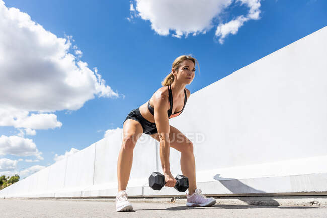 Young woman training with her dumbbell outdoors, arm down, side view — Stock Photo