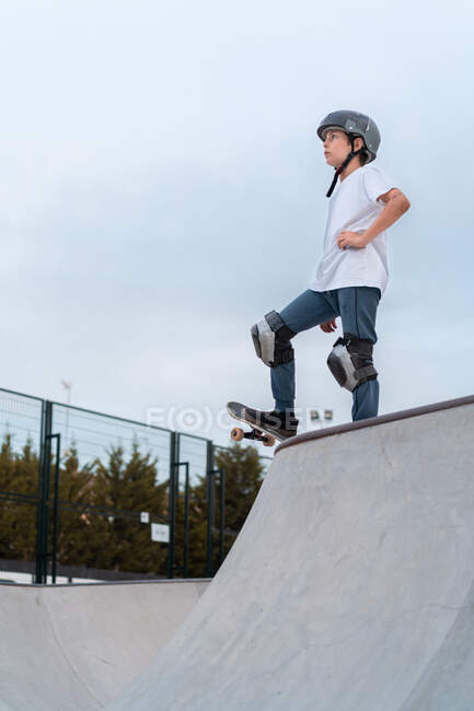 Patineur adolescent en équipement de protection équitation skateboard pendant le week-end dans le skate park et en regardant ailleurs — Photo de stock