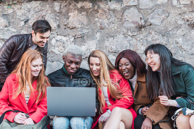 Empresa de diversos estudiantes haciendo deberes juntos mientras usan netbook en la calle de la ciudad - foto de stock