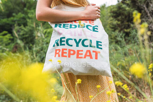 Вид сбоку на обрезанную неузнаваемую женщину, стоящую с экологически чистой текстильной сумкой в летнем парке — стоковое фото