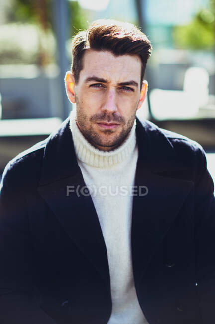 Adult bearded male in sweater and coat on the street looking at camera in city in daytime — Stock Photo