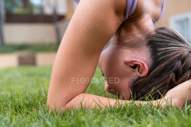 Side view of young female in sportswear standing on head with raised legs while practicing yoga in summer — Stock Photo