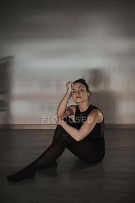 Young tender female in sports clothes touching head while sitting on floor and looking at camera — Stock Photo