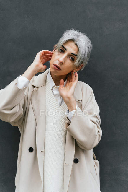 Seriöse Transgender-Frau im schicken Mantel lehnt an grauer Wand, während sie auf der Straße vor der Kamera steht — Stockfoto