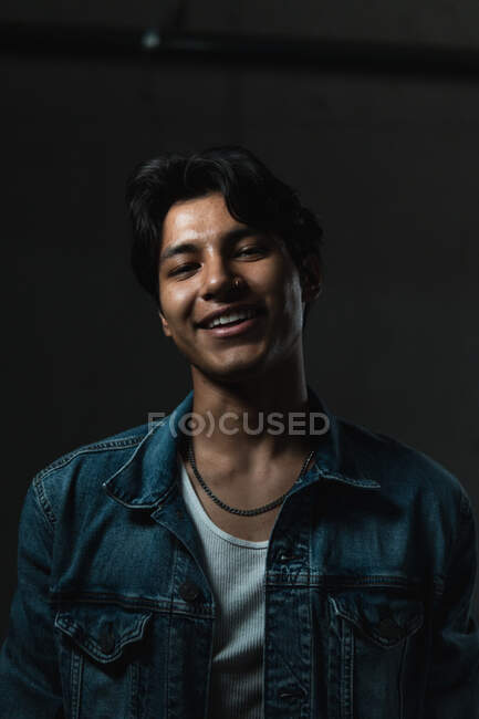 Ritratto di giovane uomo latino sorridente che guarda la macchina fotografica sotto un'illuminazione drammatica e uno sfondo scuro — Foto stock