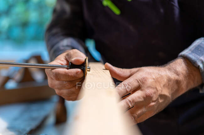Crop carpintero masculino anónimo que trabaja con el indicador profesional de marcado de ruedas y tablón de madera en el taller - foto de stock