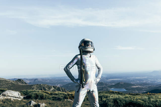 Самозабезпечений чоловічий астронавт у космосі та шоломі тримає руки на талії, стоячи на траві та каменях у високогір'ї — стокове фото