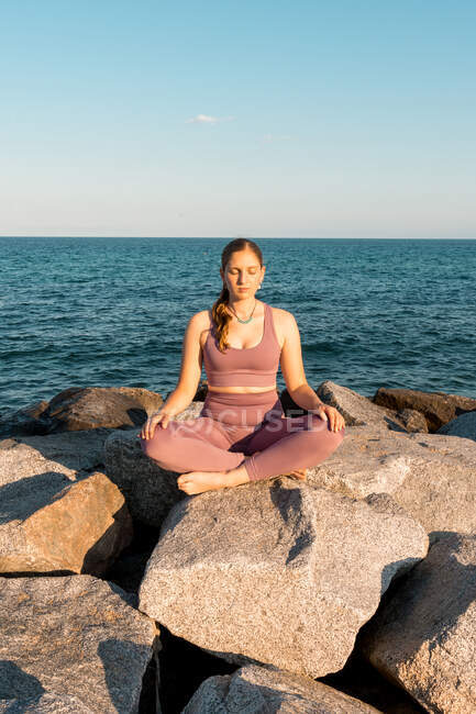 Serene female with eyes closed doing yoga in Lotus pose during meditation on rock on seashore — Stock Photo