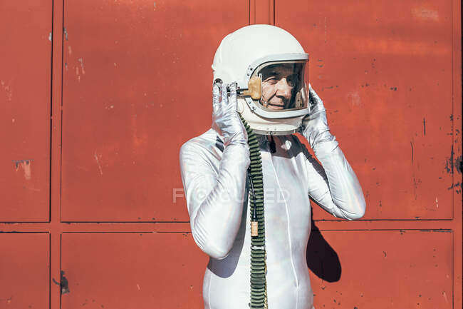 Homem no traje espacial que está perto da parede vermelha da instalação industrial no dia ensolarado — Fotografia de Stock