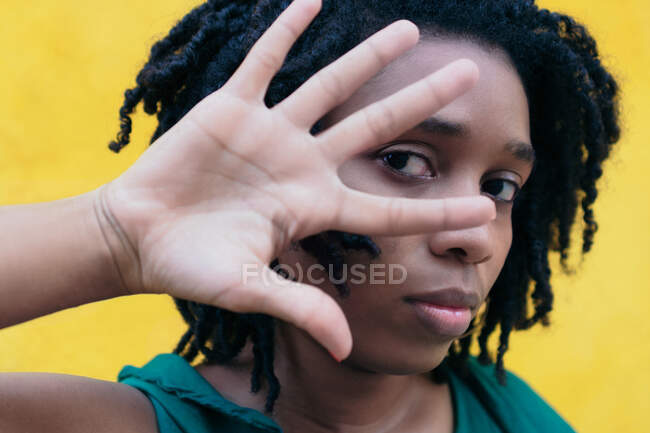 Portrait d'une jeune fille africaine élégante couvrant son visage devant un mur jaune. — Photo de stock