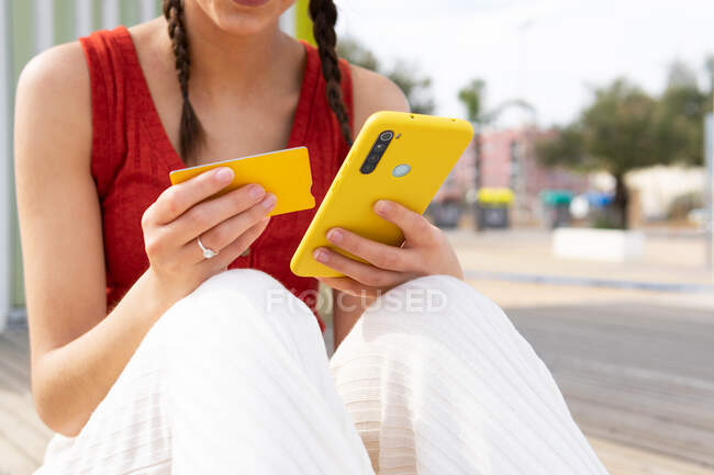 Crop view of anonymous female paying for order with plastic card during online shopping via smartphone while sitting on street — Photo de stock