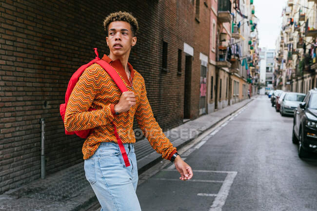 Confident young ethnic male tourist looking away while exploring old narrow streets of Barcelona city — Stock Photo