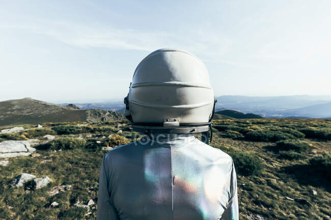 Espalda vista astronauta macho en traje espacial y casco de pie sobre hierba y piedras en las tierras altas - foto de stock