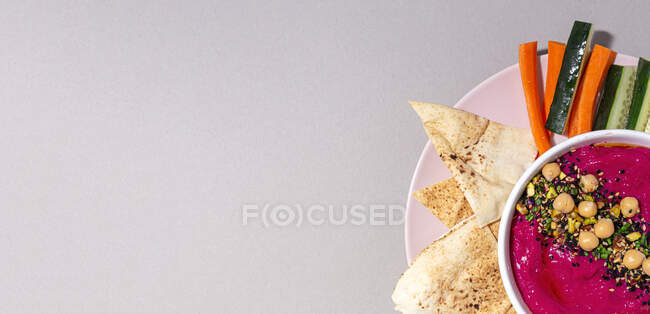 Vista superior do hummus de beterraba apetitoso decorado com grão de bico servido com pão e cenoura fresca e paus de pepino — Fotografia de Stock