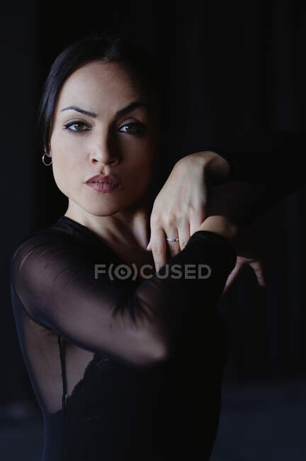 Молода витончена жінка в чорному одязі танцює фламенко з піднятими руками, дивлячись на камеру. — стокове фото