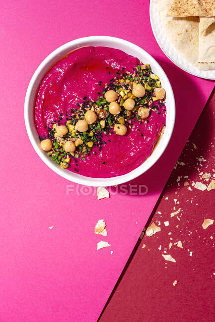 Top view of appetizing beetroot hummus garnished with chickpea served on two colored background with bread — Stock Photo