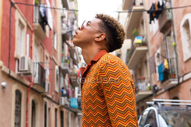Visão lateral de baixo ângulo de confiante jovem turista étnico masculino olhando para longe enquanto explora antigas ruas estreitas da cidade de Barcelona — Fotografia de Stock