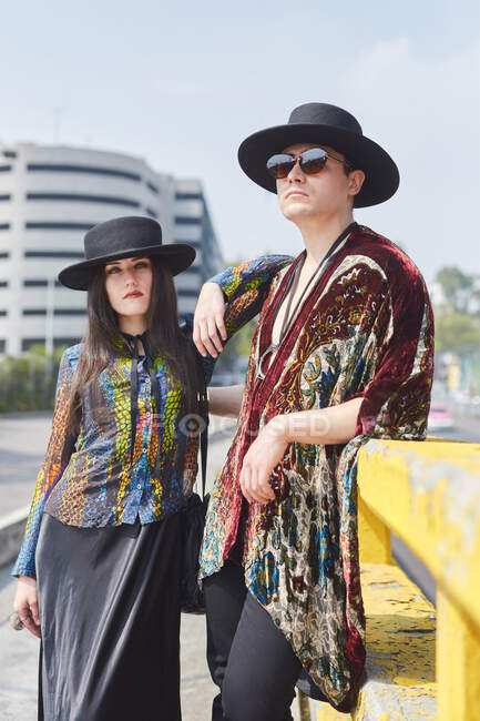 Seria pareja con estilo en ropa hipster de pie mirando a la cámara a lo largo de la calle en verano - foto de stock