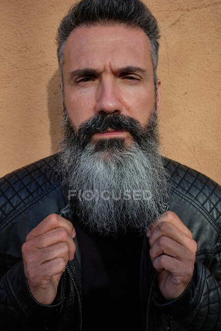 Schöner reifer Mann mit grauem Bart auf braunem Hintergrund im Studio vor laufender Kamera — Stockfoto