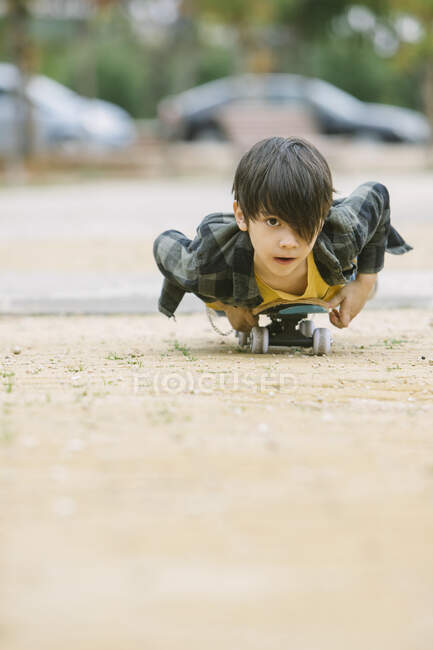 Ground level of skilled boy in casual outfit lying on skateboard while riding on sidewalk of street against blurred background — Stock Photo