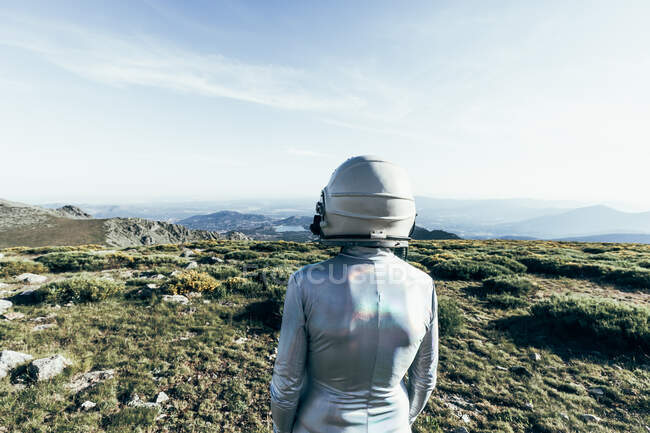 Visão traseira astronauta masculino em traje espacial e capacete em pé na grama e pedras em terras altas — Fotografia de Stock