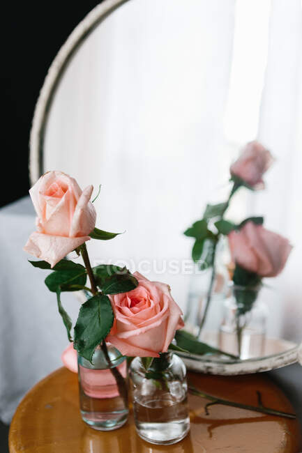 Roses roses à l'intérieur de vases en verre placés sur une table en bois sur fond neutre — Photo de stock