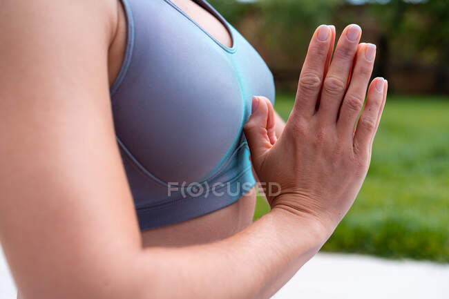 Вид збоку обрізаної невпізнаваної усвідомленої жінки з молитовними руками, що практикують йогу проти дерев вдень — стокове фото