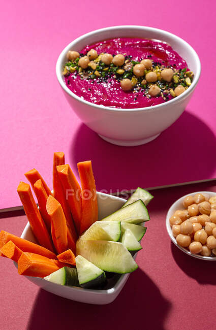 Сверху аппетитный свекольный хумус, украшенный горохом, подается на двух цветном фоне с хлебом и свежей морковью и огуречными палочками. — стоковое фото