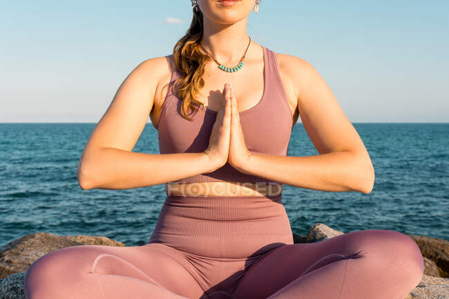 Cropped unrecognizable serene female with eyes closed doing yoga in Lotus pose during meditation on rock on seashore — Stock Photo