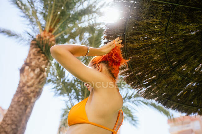 Vista posterior de ángulo bajo de la joven pelirroja anónima parada en la playa en un día soleado en verano - foto de stock