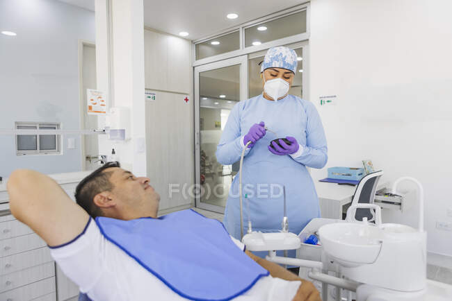 Femme stomatologue en uniforme avec outil médical se préparant pour la procédure dentaire contre l'homme à l'hôpital — Photo de stock