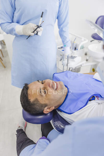 Чоловік, який посміхається, розмовляє з лікарями у формі після стоматологічної процедури в клініці. — стокове фото
