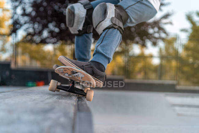 Crop Teenage boy jumping with skateboard and showing stunt on ramp in skate park — Stock Photo
