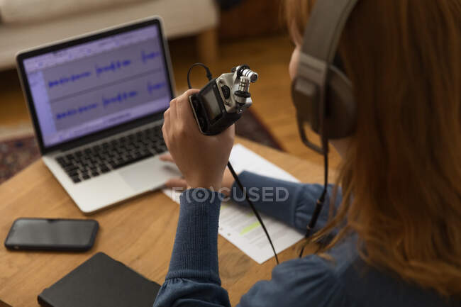 Side view of cropped unrecognizable female in headphones recording podcast while speaking in microphone and using laptop at home — Stock Photo