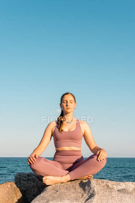 Gelassene Frau mit geschlossenen Augen beim Yoga in Lotus-Pose während der Meditation auf einem Felsen am Meeresufer — Stockfoto