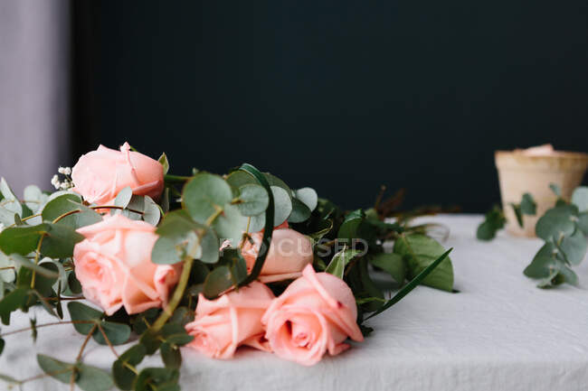 Букет из розовых роз с зелеными листьями, лежащими на белом столе — стоковое фото