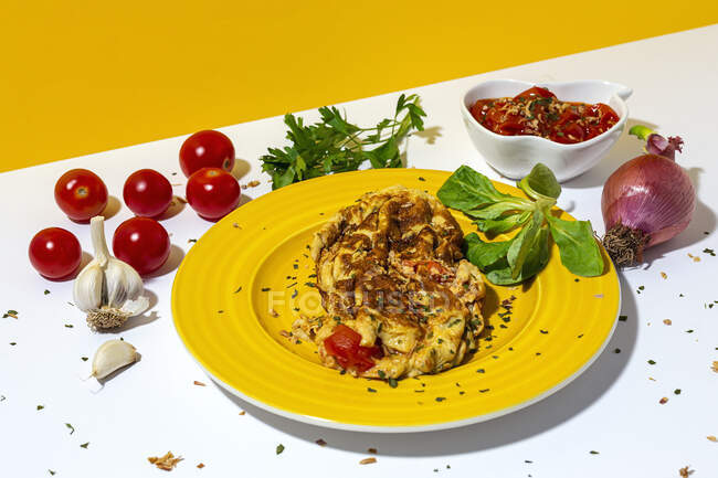 Délicieuse omelette au persil haché sur assiette contre les tomates séchées au soleil et l'oignon rouge cru sur fond bicolore — Photo de stock