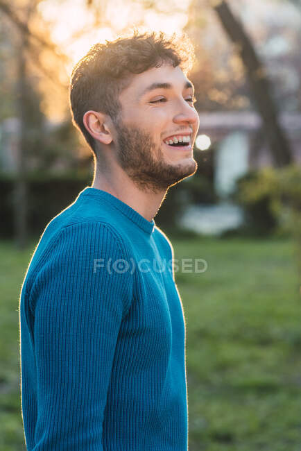 Side view of delighted handsome male smiling while spending weekend in park and looking away — Stock Photo