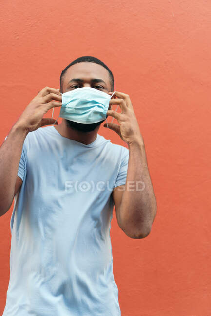 Портрет молодого чоловіка перед червоною стіною в медичній масці, щоб захистити себе від спалаху коронавірусу, ковадла-19 . — стокове фото