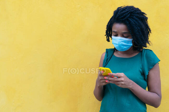 Porträt einer jungen Frau mit Schutzmaske, die auf der Straße eine Smartphone-Nachricht sendet. Pandemiekonzept — Stockfoto