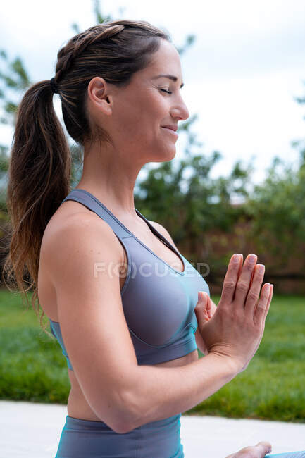 Side view of young mindful female with crossed legs and closed eyes practicing yoga against trees in daytime — Stock Photo