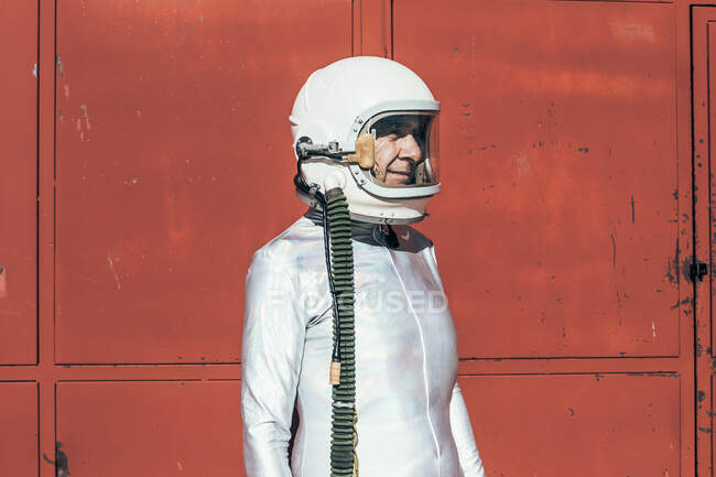 Людина в космосі стоїть біля червоної стіни промислового об'єкта в сонячний день — стокове фото