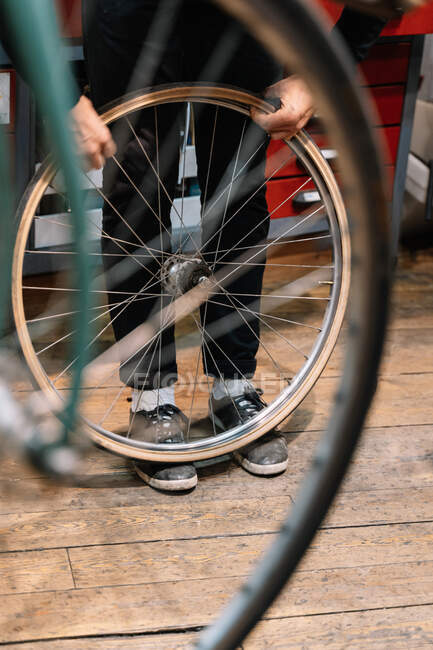 Low angle of anonymous male mechanic repairing wheel of bicycle while working in workshop — Stock Photo