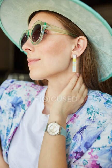 Cheerful young female in trendy wear with sunglasses against rough wall in town — Stock Photo