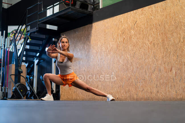 Basso angolo corpo pieno di atleta femminile in forma in abbigliamento sportivo facendo esercizio affondo laterale in palestra — Foto stock