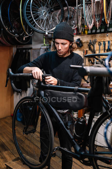 Manillar masculino serio de la fijación del mecánico de la bicicleta mientras que trabaja en taller del servicio de reparación - foto de stock