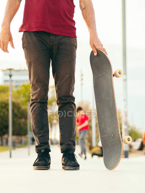 Неузнаваемый скейтбордист, стоящий на тротуаре под солнечным светом на городской улице. — стоковое фото